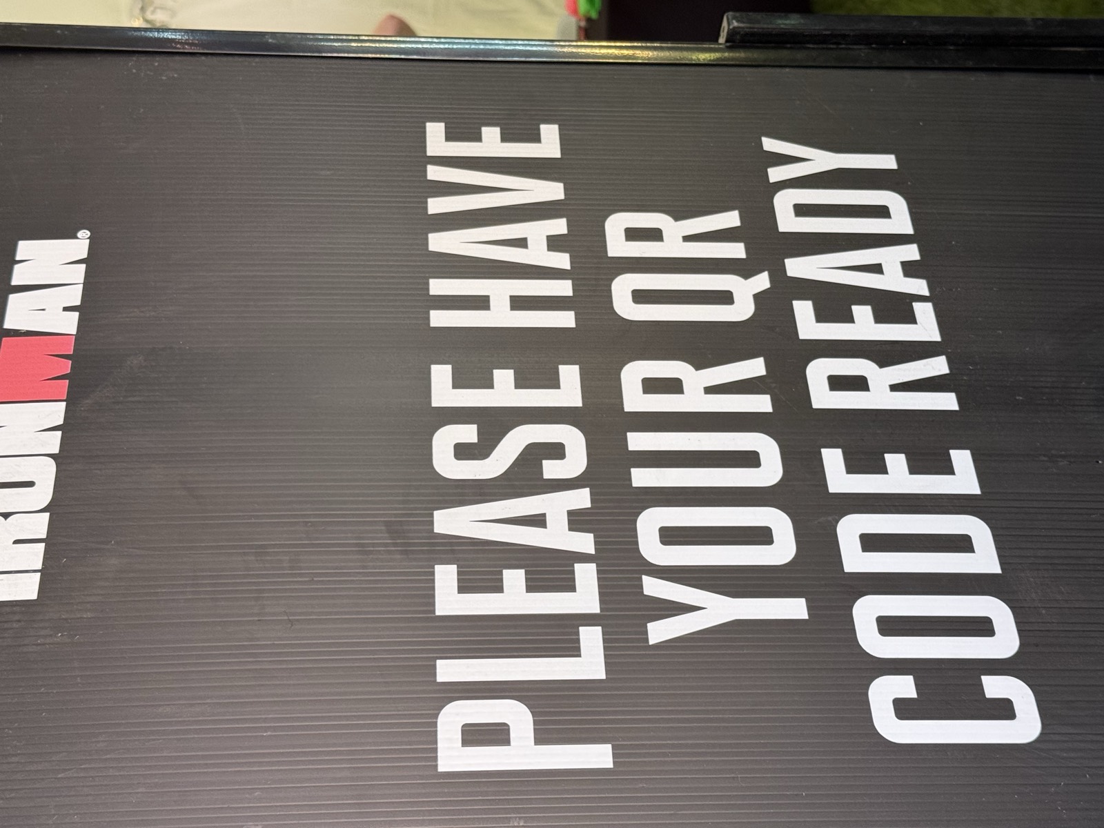 A signboard at athlete check-in reading "PLEASE HAVE YOUR QR CODE READY"